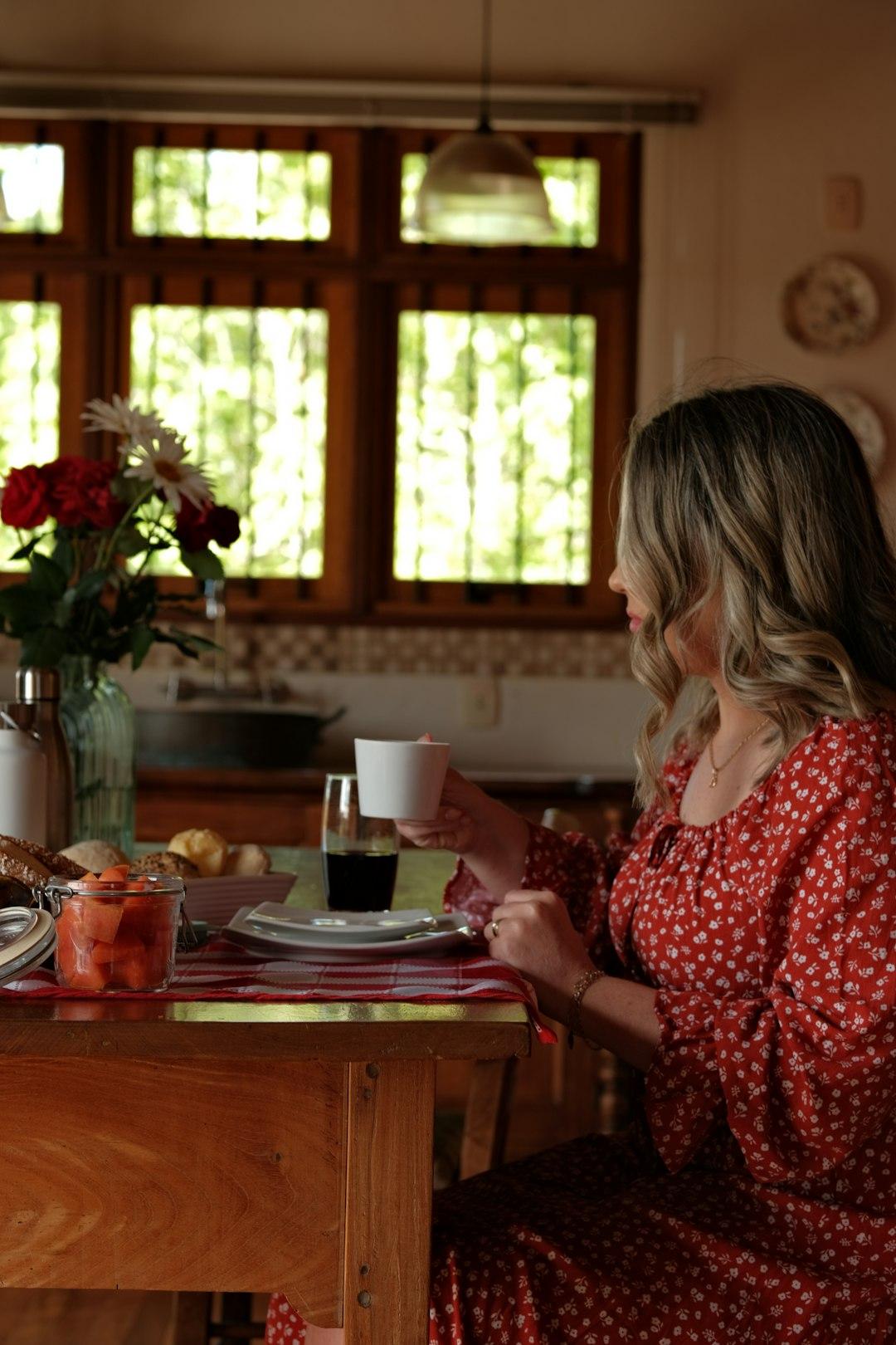 Mulher tomando café com calma na cozinha pela manhã, sem precisar ligar para confirmar horários.